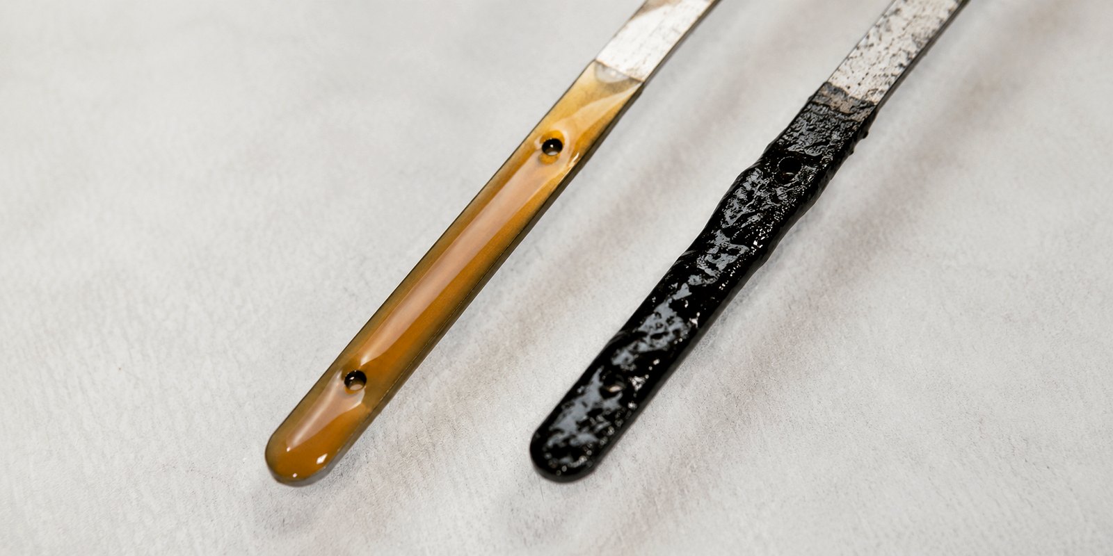 Two dipsticks side by side — clean amber oil on the left, dark dirty oil on the right