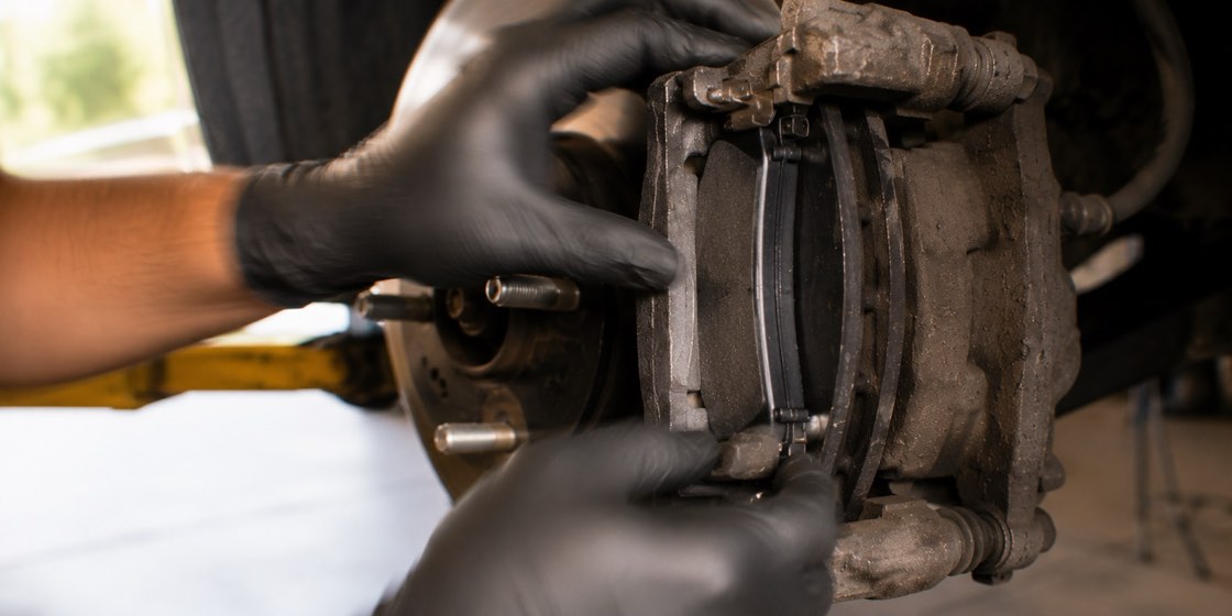 A mechanic's gloved hands fitting new brake pads into the caliper during a brake job