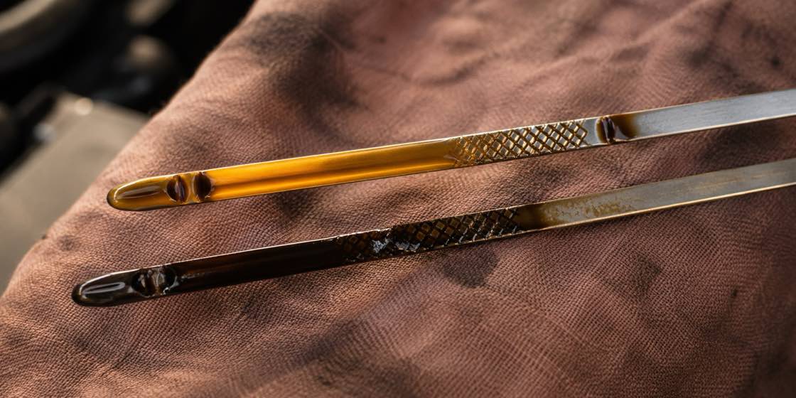 Two engine dipsticks side by side, one with clean amber oil and one with dark dirty oil