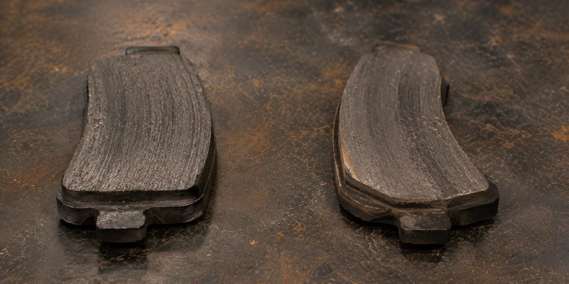 Worn brake pads laid side by side on a workbench showing how unevenly they can wear down